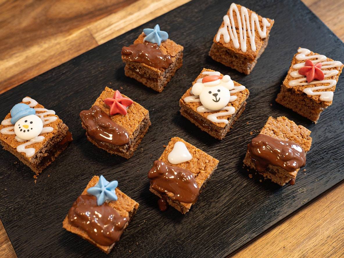 Kleine Weihnachtskuchen, verziert mit Schneemännern, Eisbären und Sternen auf einem schwarzen Tablett.