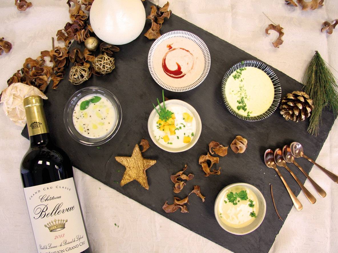 Fünf Schalen mit Suppen oder Saucen und eine Flasche Château Bellevue Wein auf Schieferplatte.