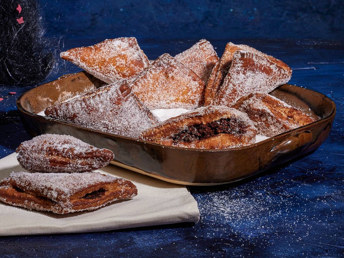 Zuckerbestreute dreieckige und längliche Krapfen, einige mit Schokolade gefüllt, in einer Schale.