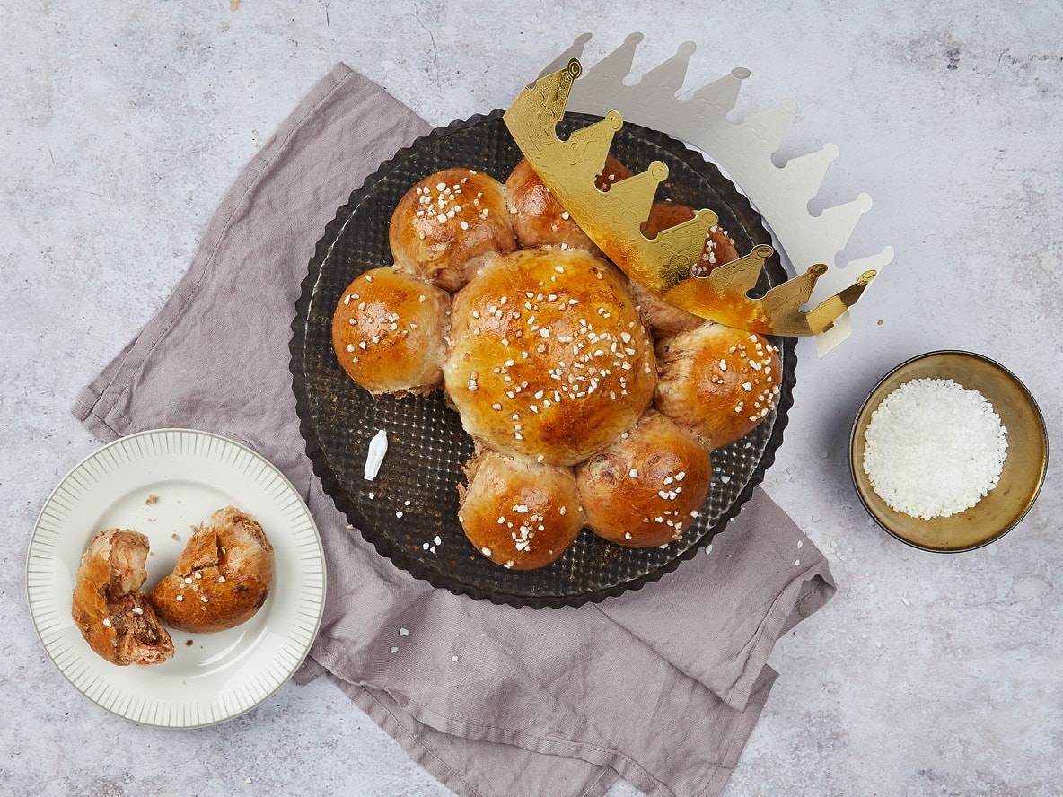 Königskuchen mit Zuckerstreuseln und einer goldenen Krone auf einem dunklen Backblech.