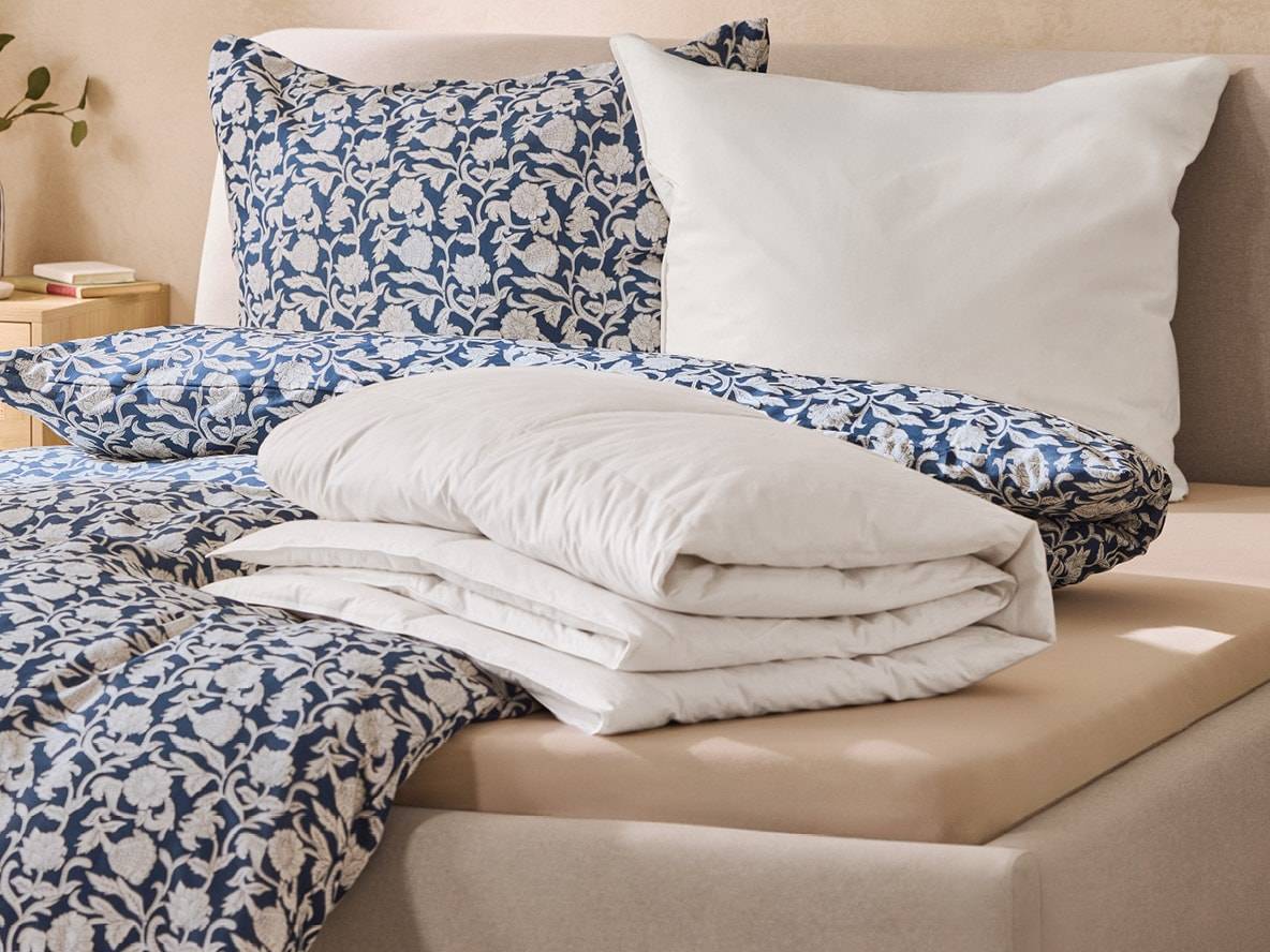 Bettwäsche-Set mit blauen Blumenmustern und weißen Kissen auf einem Bett.