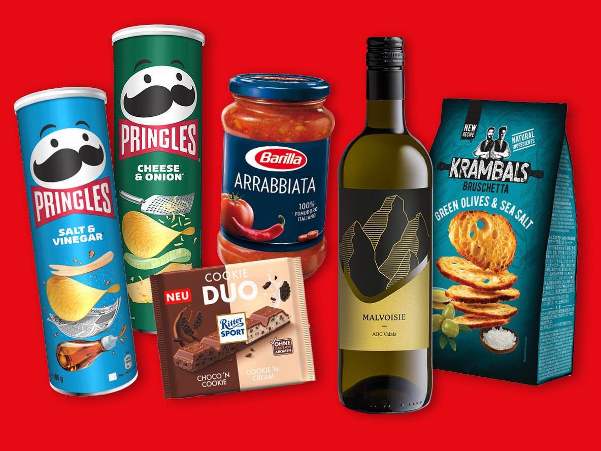Eine Auswahl an Snacks, darunter Pringles Chips, Barilla Sauce, Ritter Sport Schokolade, KRAMBALS Bruschetta und eine Flasche Malvoisie Wein.