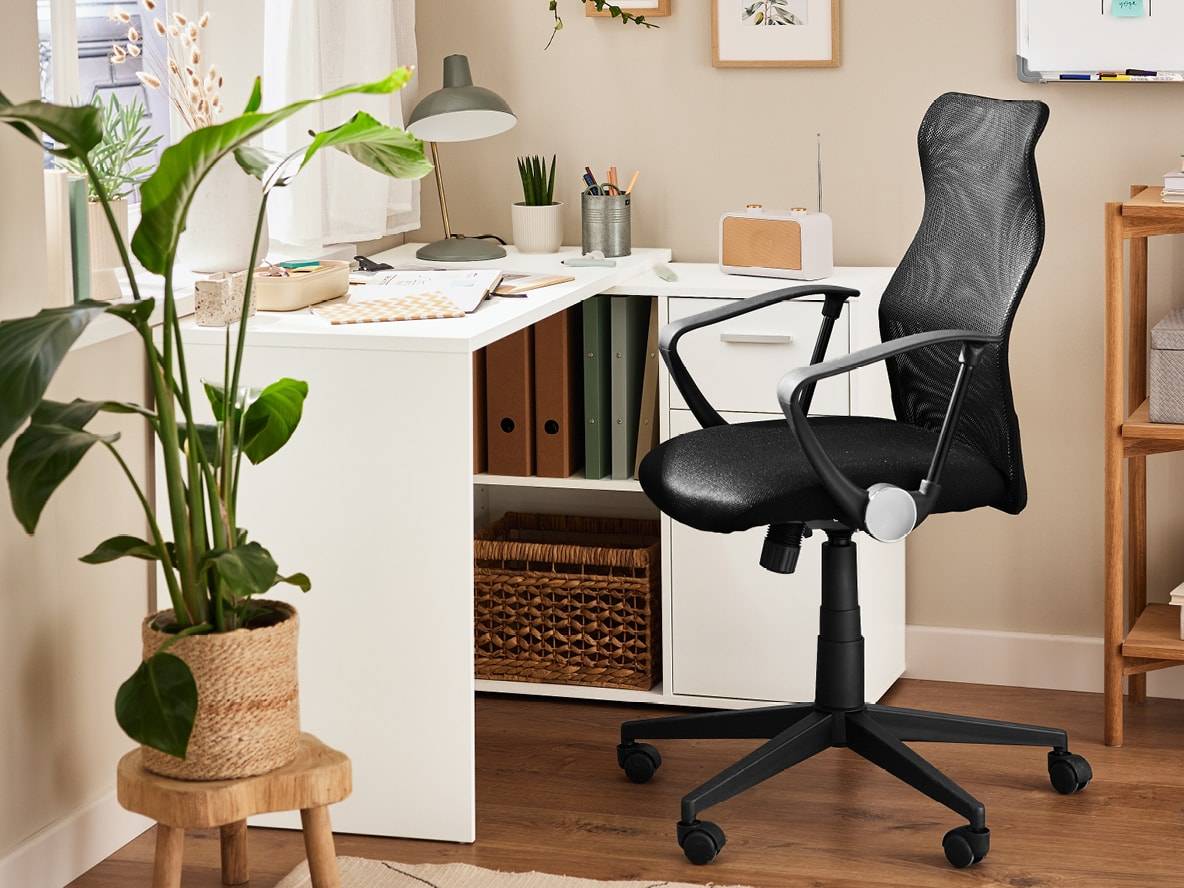 Ein weißer Schreibtisch mit schwarzem Mesh-Bürostuhl, Pflanzen und Zubehör.
