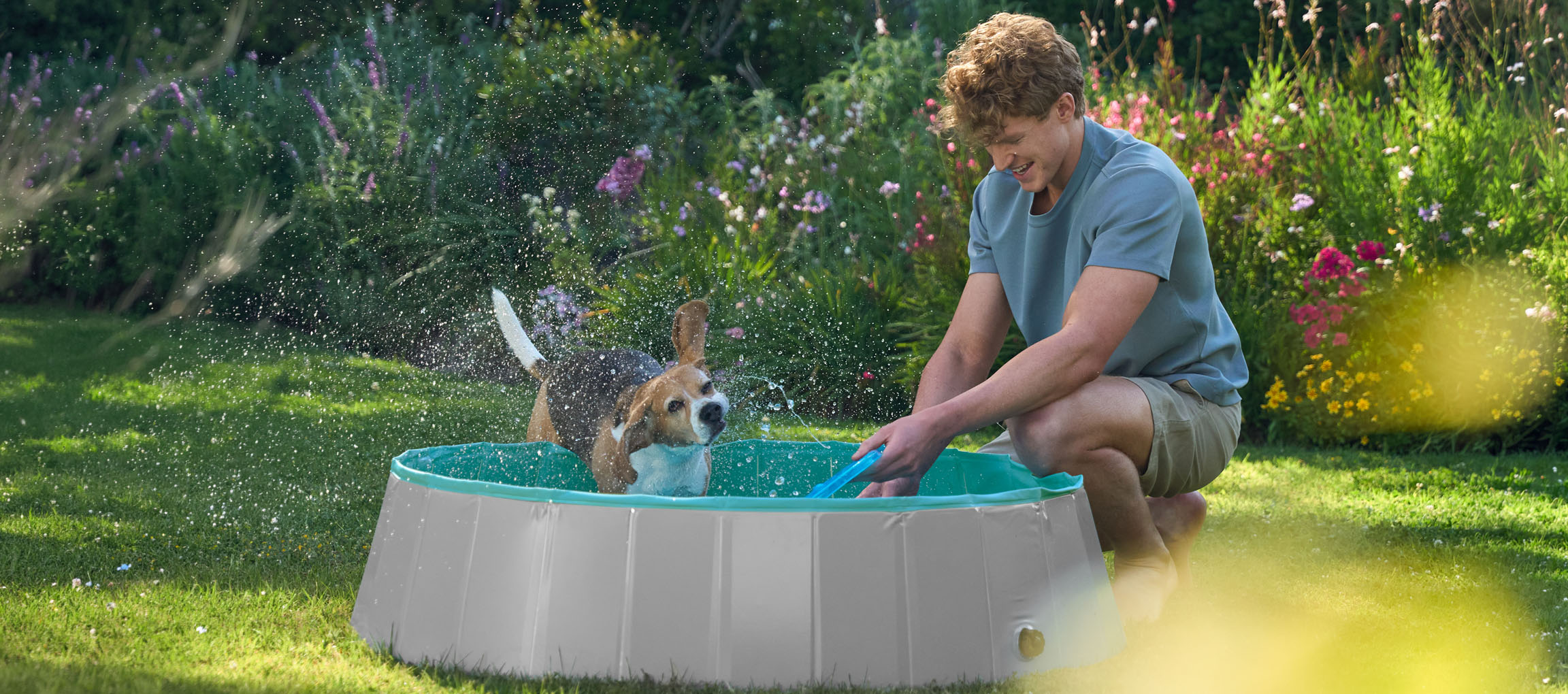 Homme et chien jouant dans une pataugeoire dans le jardin.