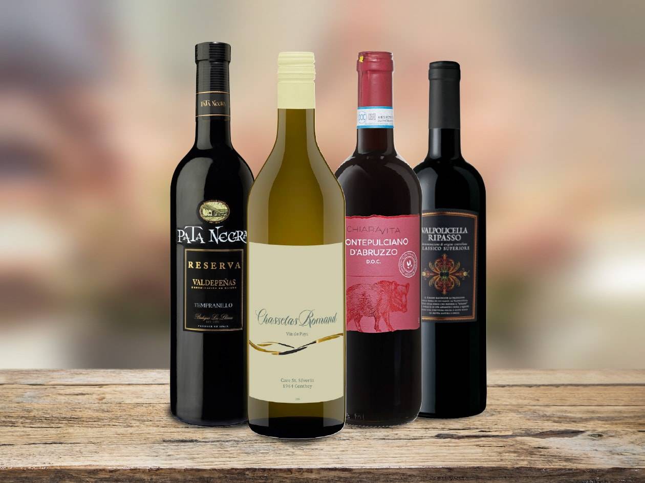 Vier Weinflaschen, darunter Pata Negra Reserva und Valpolicella Ripasso, auf einem Holztisch.