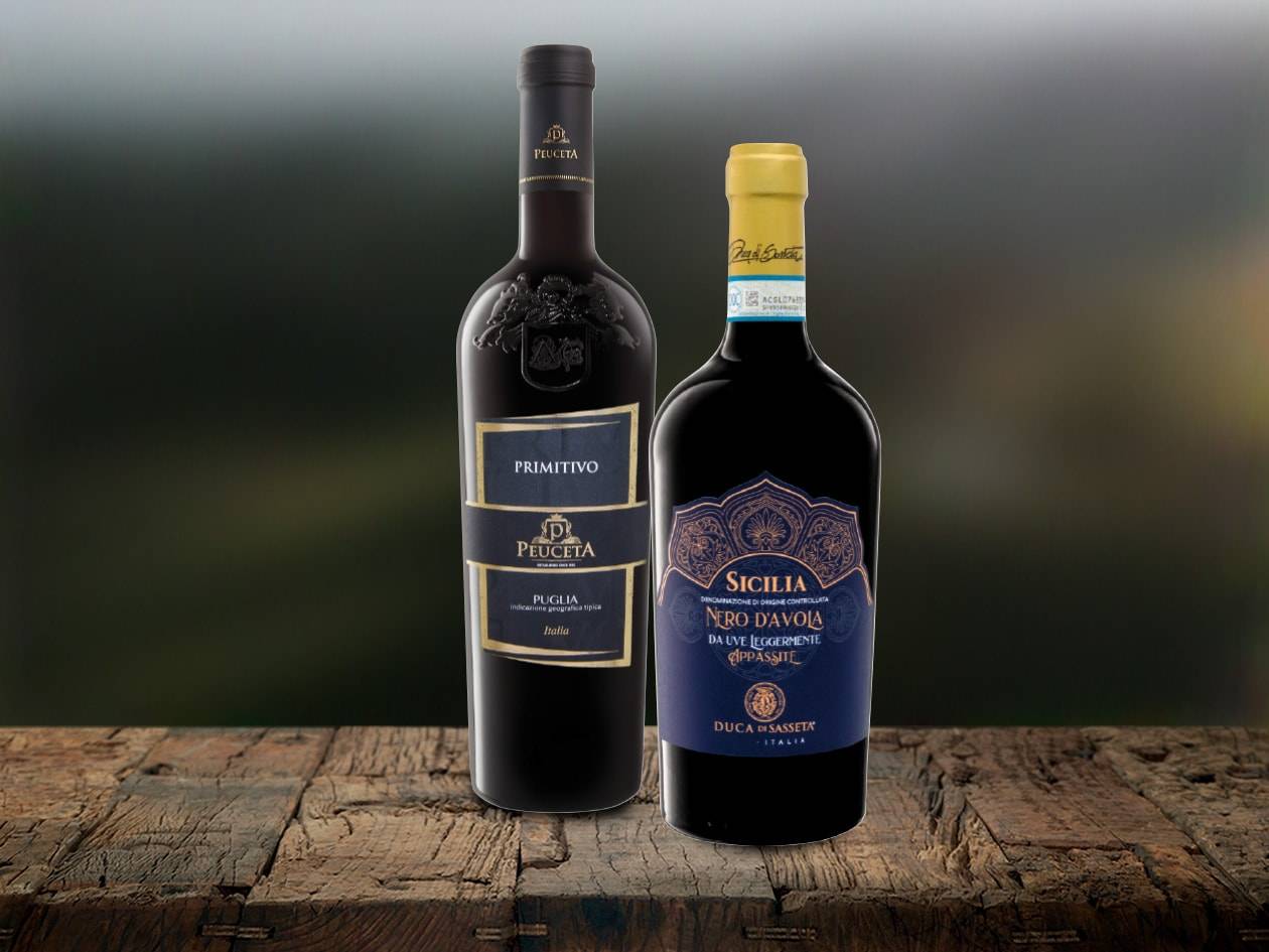Zwei italienische Weinflaschen, Peuceta Primitivo und Duca di Sasseta Nero d'Avola, stehen auf einem Holztisch.