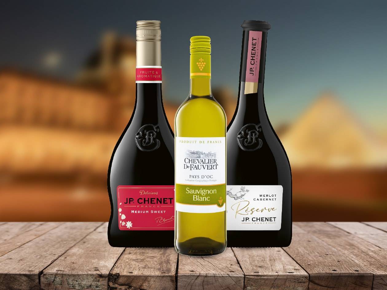 Drei Flaschen JP. Chenet Wein, darunter Rot- und Weißweinsorten, auf einem Holztisch.