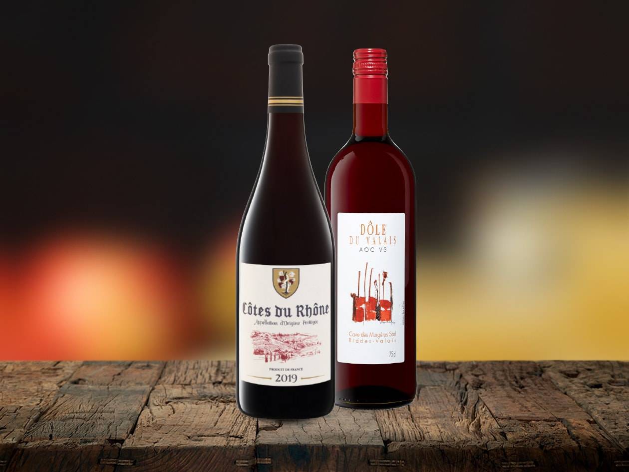 Zwei Flaschen Rotwein, Côtes du Rhône und Dôle du Valais, stehen auf einem Holztisch.