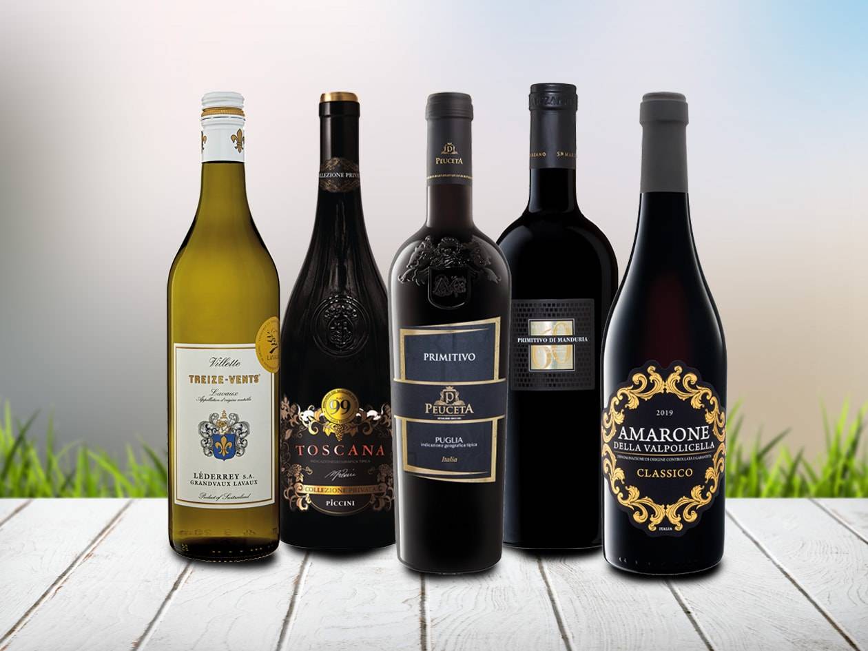 Fünf Weinflaschen, darunter ein Weißwein und vier Rotweine, auf einem Holztisch.