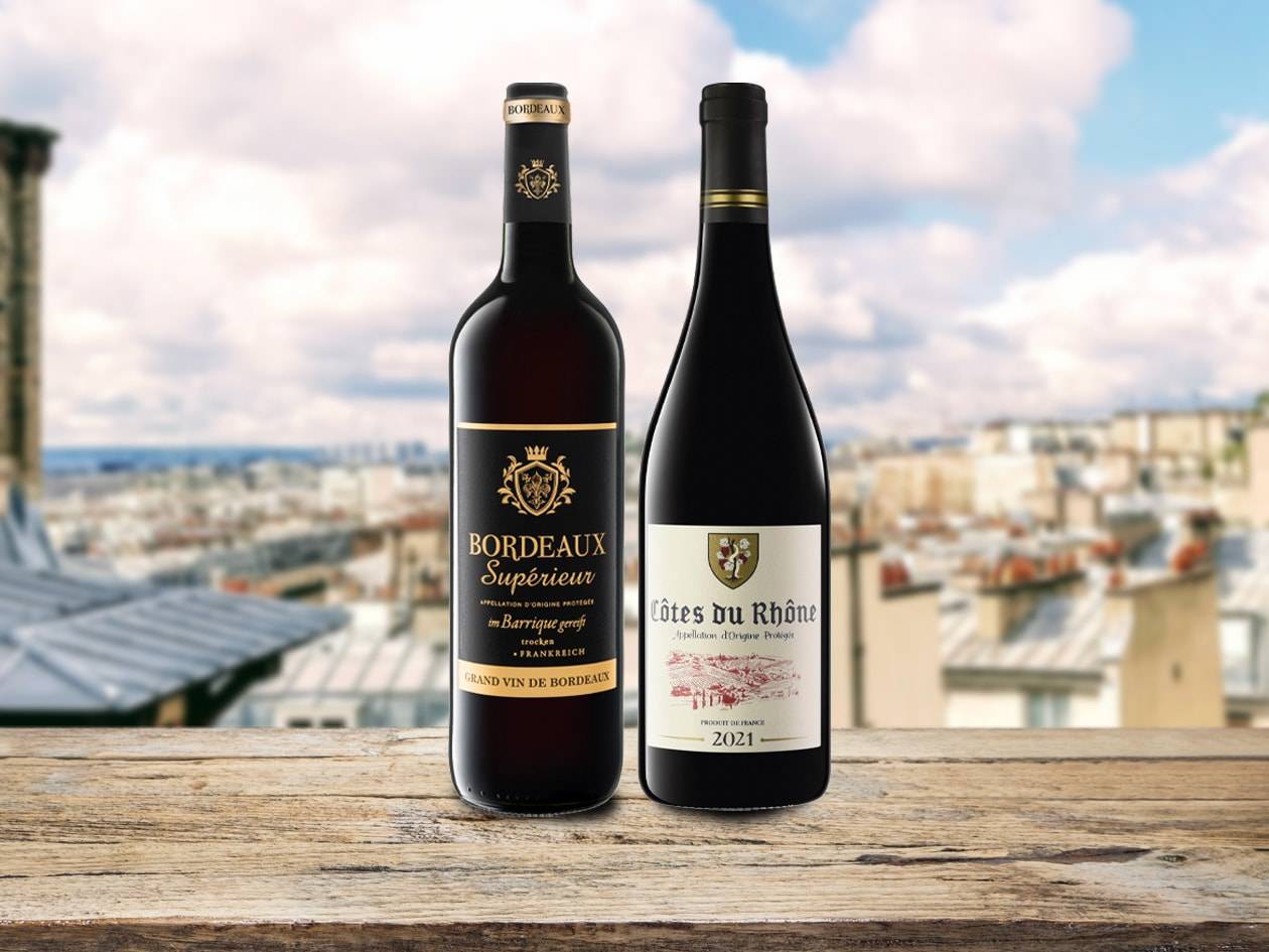 Due bottiglie di vino rosso, Bordeaux Supérieur e Côtes du Rhône, su un tavolo di legno con vista su Parigi.