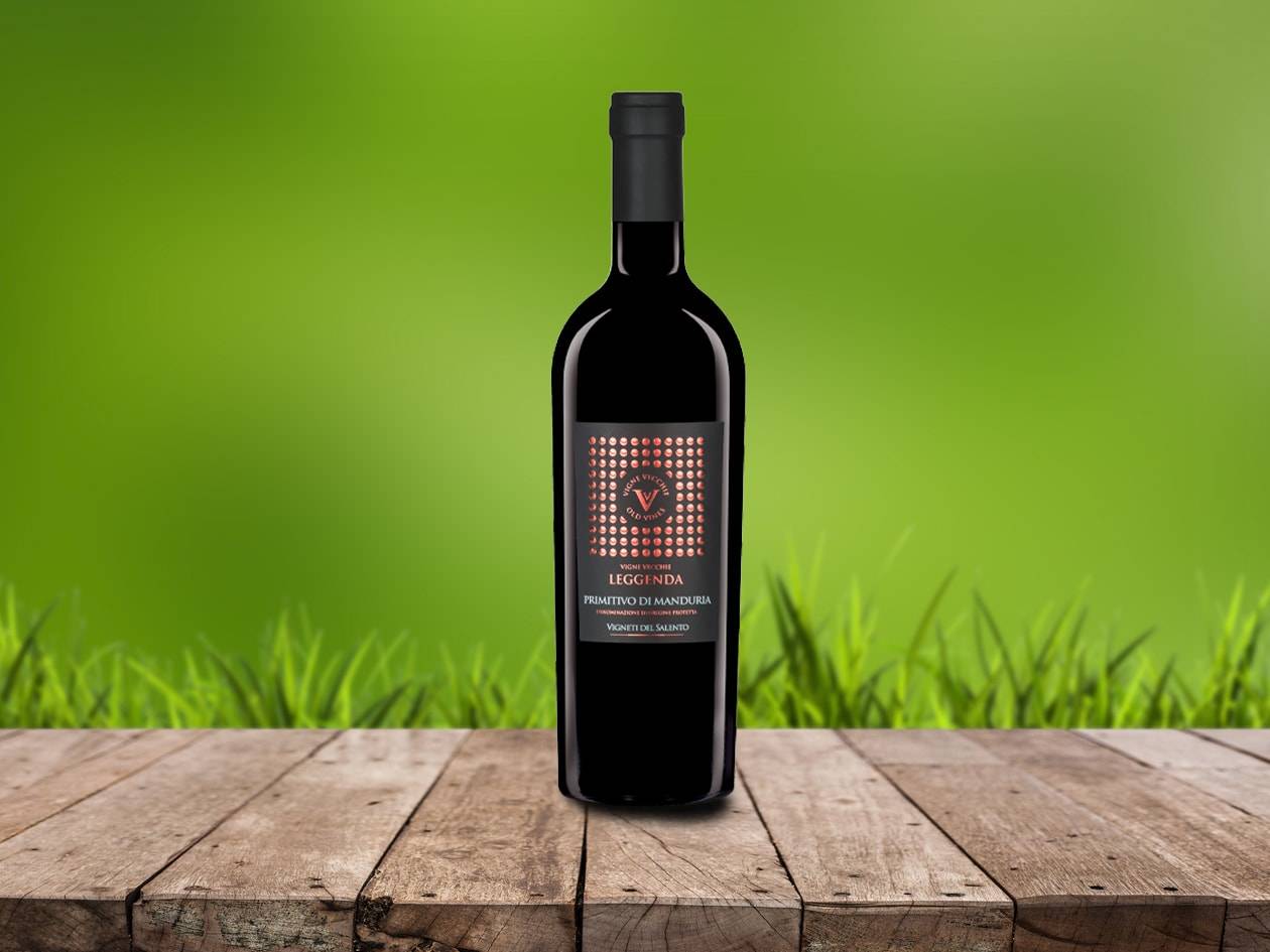 Eine Flasche Rotwein auf einem Holztisch vor verschwommenem grünem Hintergrund.