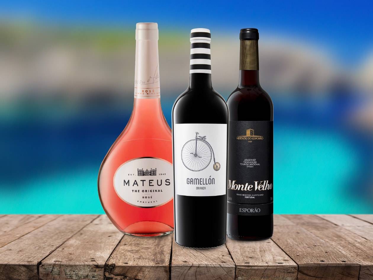 Trois bouteilles de vin, dont un rosé Mateus et deux vins rouges, sur une table en bois.