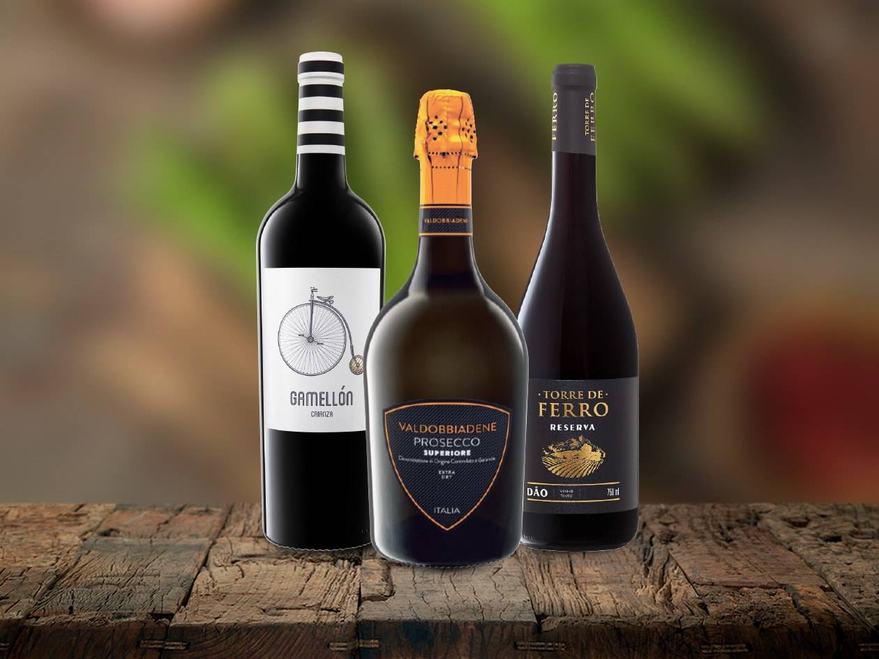 Drei Flaschen Wein und Prosecco auf einem Holztisch.