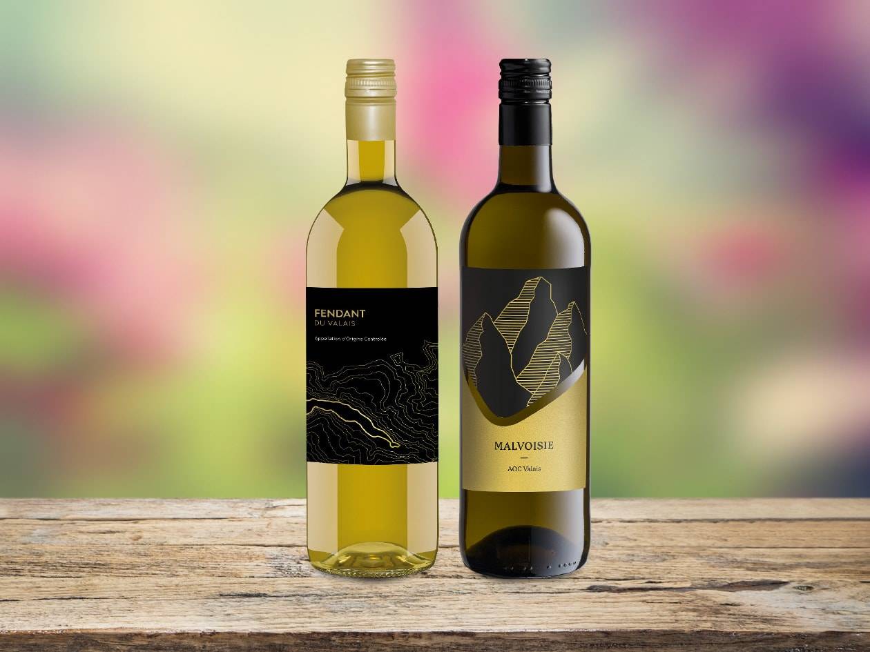 Zwei Flaschen Weißwein, Fendant und Malvoisie, auf einem Holztisch.
