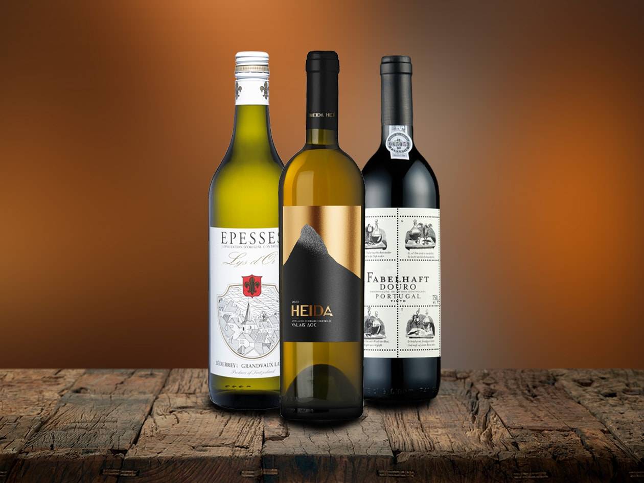 Drei Weinflaschen, zwei weiße und eine rote, auf einem Holztisch.