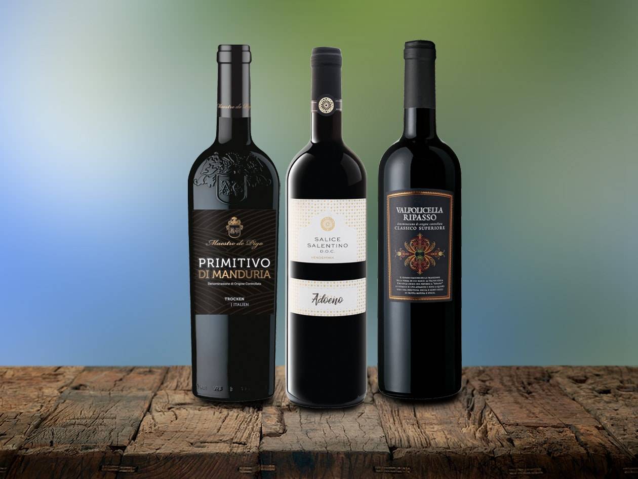 Trois bouteilles de vin rouge italien, dont un Primitivo di Manduria et un Valpolicella Ripasso, sur une table en bois.