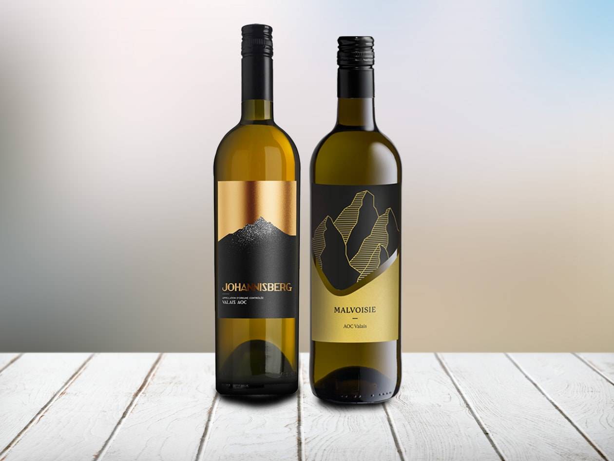 Zwei Weißweinflaschen mit schwarzen und goldenen Etiketten, die Berge zeigen, auf einem Holztisch.