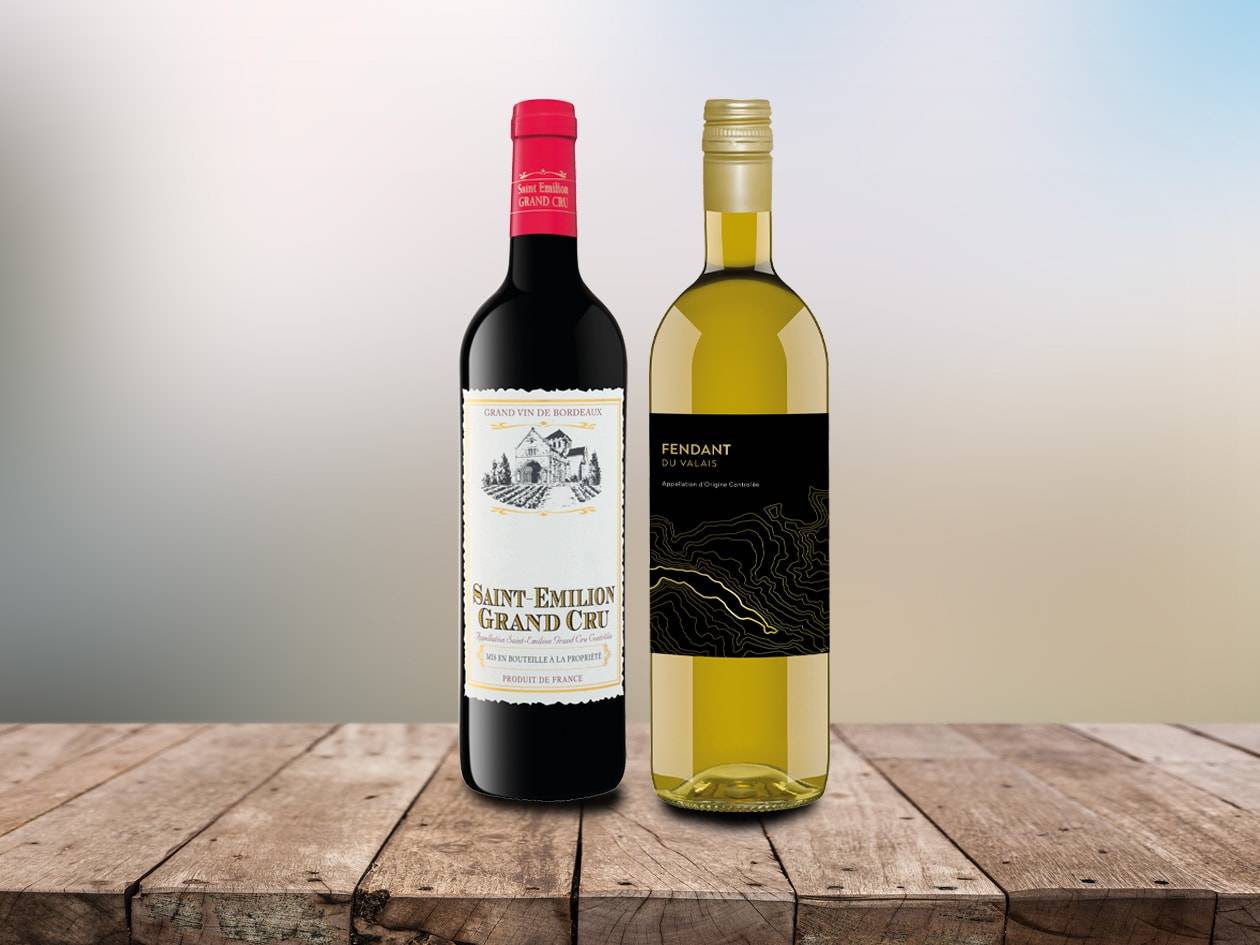 Zwei Weinflaschen, ein roter Saint-Émilion Grand Cru und ein weißer Fendant du Valais, auf einem Holztisch.