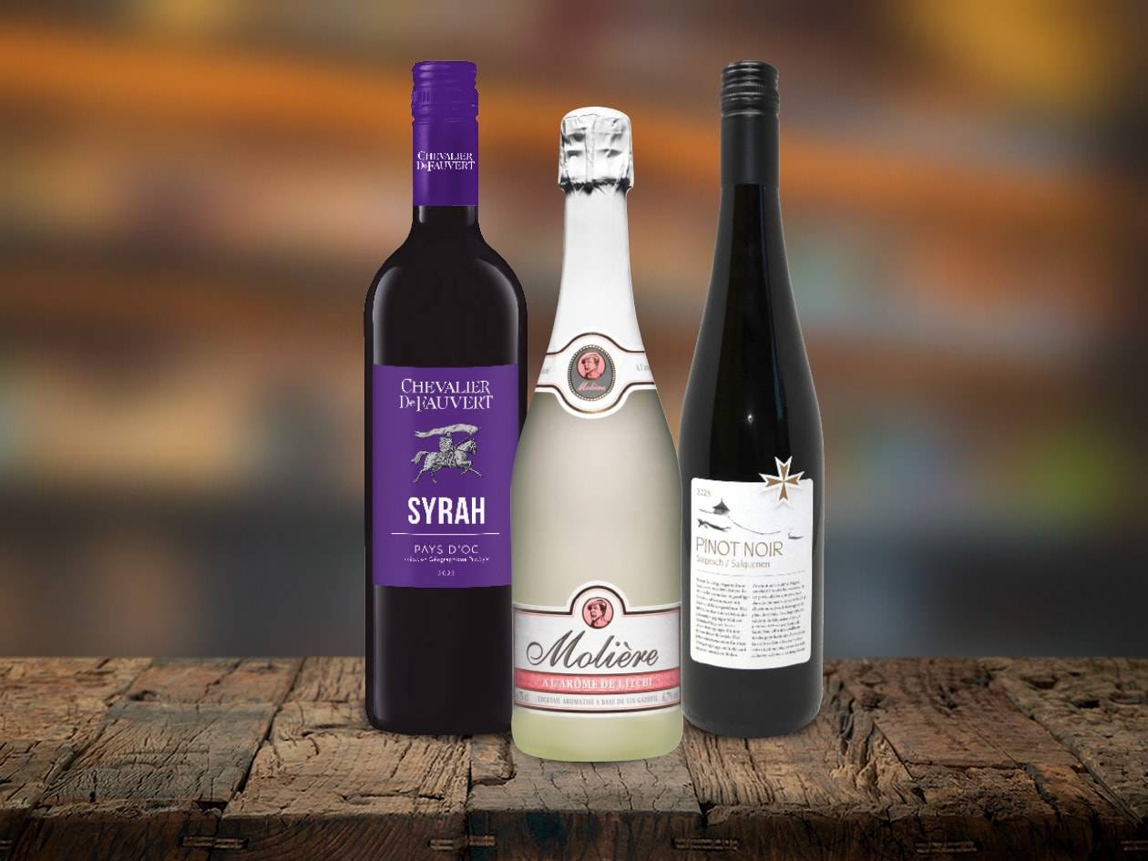 Drei Weinflaschen, darunter Syrah, Molière und Pinot Noir, auf einem Holztisch.