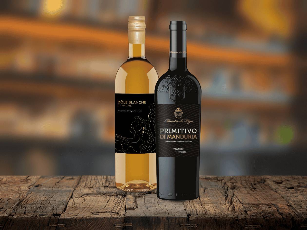 Zwei Weinflaschen, ein weißer Dôle Blanche du Valais und ein roter Primitivo di Manduria, auf einem Holztisch.